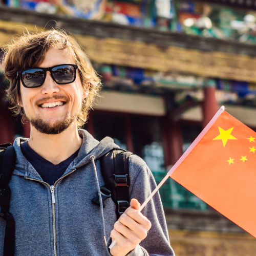 Turista sonriente con bandera de China frente a arquitectura tradicional tibetana, viaje personalizado por China